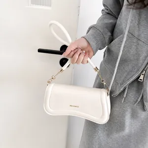 Detail of creamy white shoulder bag with gold lettering and metallic chain buckle