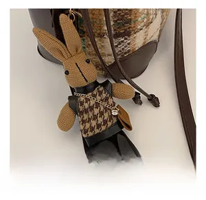 Knitted rabbit bag charm with houndstooth vest and gold chain on a bucket bag