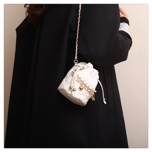 Close-up of white quilted bucket bag with gold heart charm and chain leather strap
