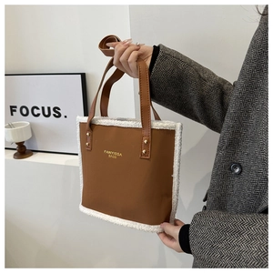 Detail of faux shearling trim on brown leather tote bag held by model in minimalist setting