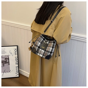 Detail of plaid bucket bag featuring a brown bear charm on a khaki trench coat