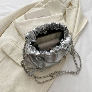 Silberne Beuteltasche mit Kordelzug, Kette und Schleifen-Detail auf beige Sakko