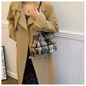 Detail view of a plaid tweed bucket bag with black leather trim and a rabbit charm