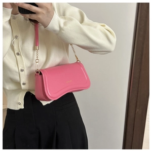 Detail view of bright pink leather shoulder bag with unique wave-curved base and gold chain