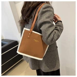 Brown tote bag with white faux shearling trim and gold logo shown on model's shoulder