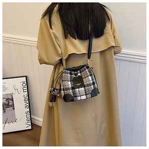 Detail of checkered bucket bag with leather trim and bear charm on trench coat model