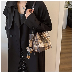 Detail of tweed bucket bag with leather trim and cute rabbit doll pendant on black coat