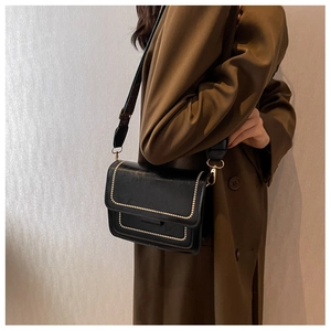 Close-up of black crossbody bag with gold studs and wide strap on a brown coat
