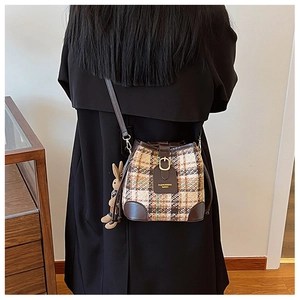 Plaid bucket bag with leather trim and plush rabbit charm shown on a shoulder