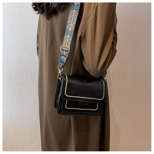 Detail of black crossbody bag with gold studs and colorful ethnic jacquard strap