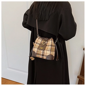 Detail of plaid tweed bucket bag with leather trim and gold buckle worn by model
