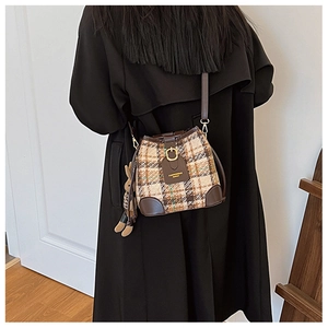 Detail of retro plaid bucket bag with plush rabbit charm worn over a black outfit