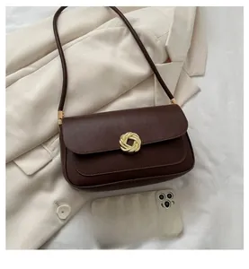 Detail of a brown leather shoulder bag with a gold metal buckle on a beige blazer