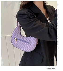 Detail of light purple woven crescent bag with gold zipper on a black blazer background