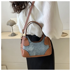 Detail of a contrast patchwork shoulder bag with brown leather and blue denim texture strap