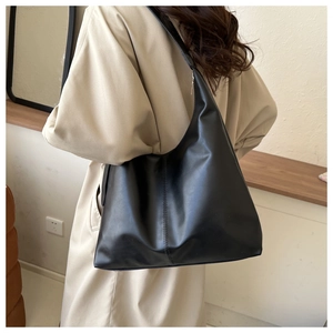 Detail of a large black matte leather tote bag with double stitching on a beige coat