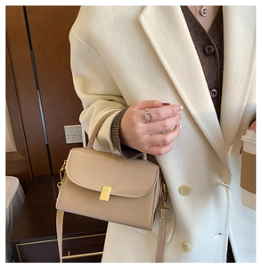 Detail of beige square crossbody bag with gold rectangular buckle and elegant flap closure