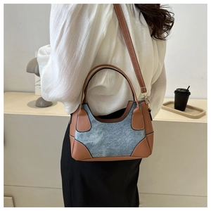Detail view of contrast stitching and blue denim paneling on a chic baguette bag