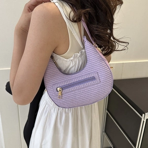 Purple woven crescent shoulder bag with gold zipper shown on a model in white dress