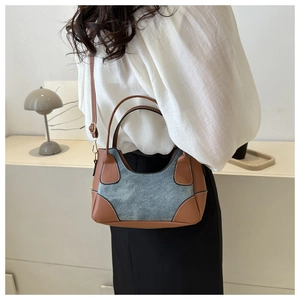 Detail of color-block baguette bag with leather handles and denim texture panels