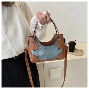 Detail of contrasting brown leather and blue denim stitching on a stylish shoulder bag