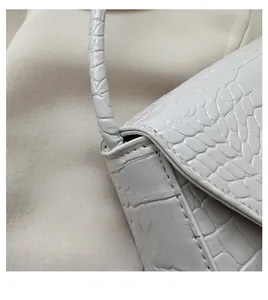 Detailed close-up of stitching and crocodile embossed leather on a beige crossbody bag