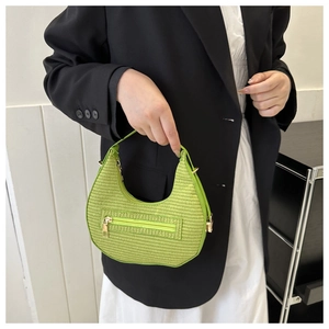 Close-up of bright green woven crescent bag with gold zipper and metal hardware detail