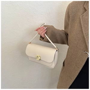 Detail of cream shoulder bag featuring a stylish golden twisted knot metal buckle clasp