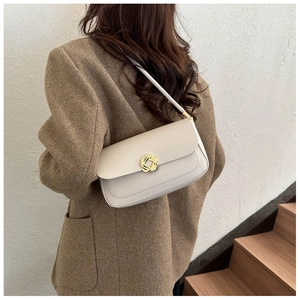 Detail showing the creamy beige shoulder bag featuring a gold woven circular metal buckle