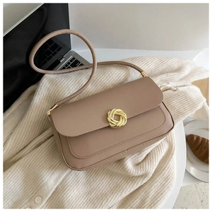 Detail of dusty pink leather crossbody bag with a unique gold circular buckle on knitwear