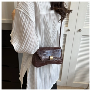 Detail of dark brown faux crocodile skin texture and gold buckle on a shoulder bag
