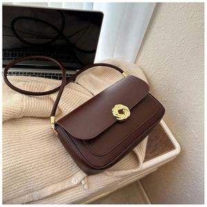 Close-up of a brown leather shoulder bag with a gold spiral metal buckle on a knit cardigan