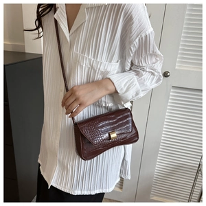 Detail of dark brown crocodile pattern leather crossbody bag on white pleated shirt