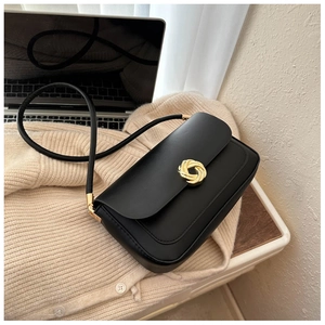 Minimalist black leather square shoulder bag with vintage gold hardware on beige knitwear