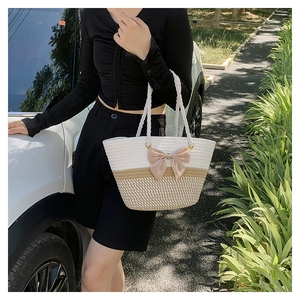 Close-up of woven straw tote bag with beige stripes, satin bow, and thick rope handles