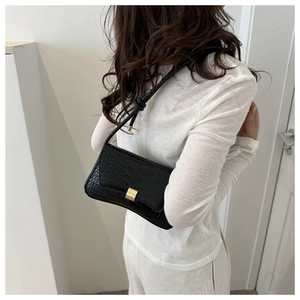 Detail of black faux crocodile leather baguette bag with a golden metal buckle closure