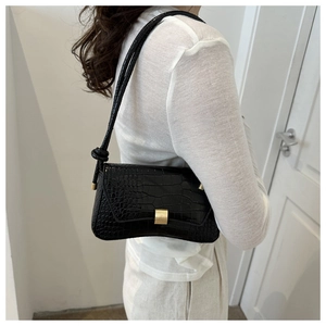 Detail of black faux leather baguette bag with crocodile texture and gold metal buckle