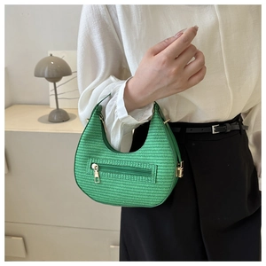 Detail of green woven crescent bag with gold zippers worn in a minimalist setting