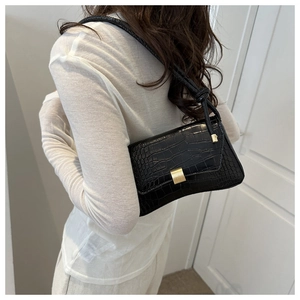 Detail of black crocodile texture shoulder bag with gold metallic buckle and knotted strap