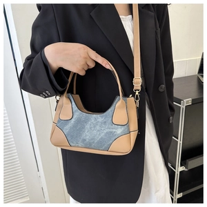 Detail shot of vintage denim and brown leather patchwork baguette bag on a model