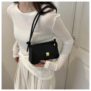 Detail of black crocodile texture shoulder bag with gold buckle and knotted strap