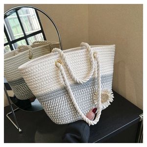 Detail of hand-woven tote bag with white and grey gradient patterns and daisy charm