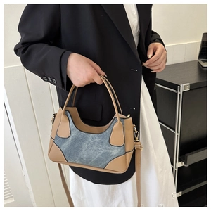 Detail of color-block patchwork underarm bag showing brown leather and denim texture