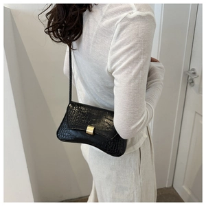 Detail view of the curved base and golden buckle on a black crocodile pattern crossbody bag