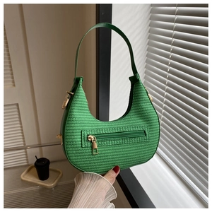 Detail of green woven crescent bag showing metallic zipper and texture under sunlight