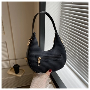 Close-up of black woven crescent bag with gold zipper detail and metallic hardware