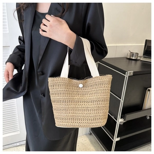 Detail view of a woven straw handbag with white fabric handles and button closure