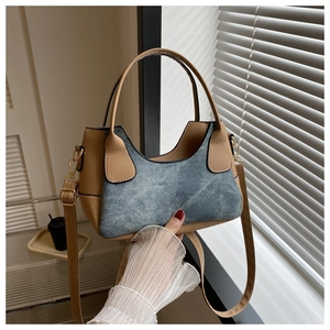 Detail of color-block underarm bag with blue denim texture and brown leather strap
