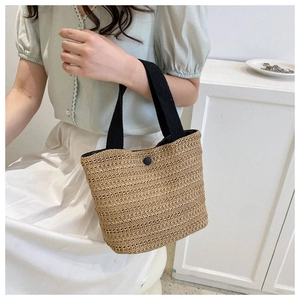 Detail of hand-woven straw tote bag with black canvas straps and button closure