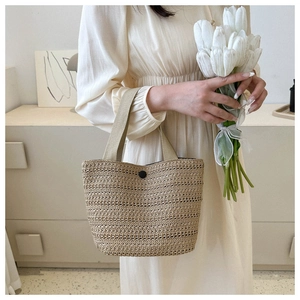 Close-up of a woven straw tote bag with a black button detail and fabric handles